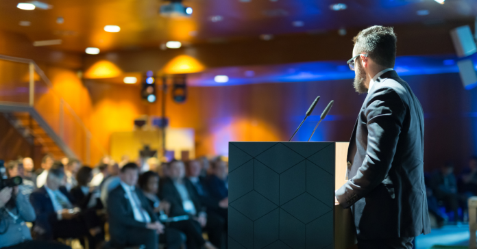 Keynote speaker onstage at a podium addressing a group of business professionals