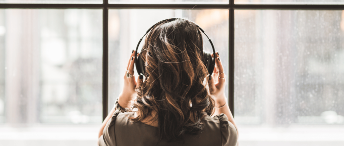 A woman listens to a podcast while looking outside a window