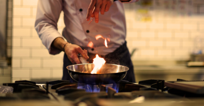 A chef in a kitchen cooking with a pan