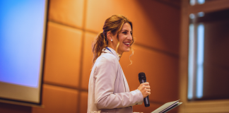 Keynote speaker smiling on stage with a microphone and notes