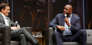 Magic Johnson sits on stage with a microphone