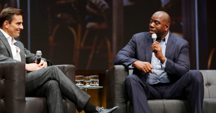 Magic Johnson sits on stage with a microphone