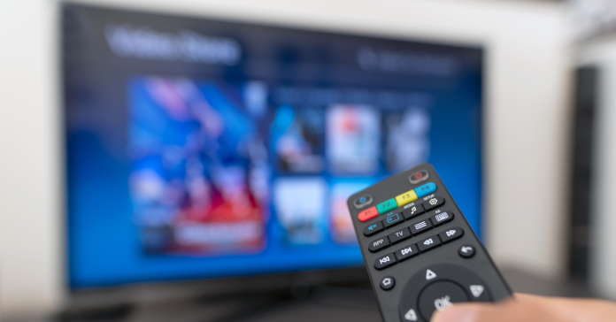 TV remote being held up in front of a TV screen